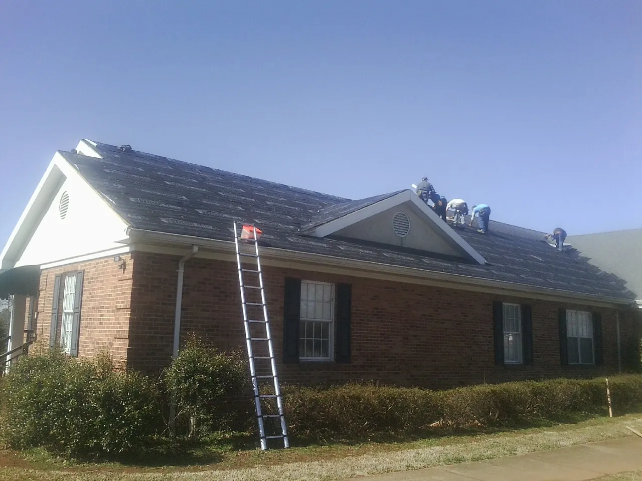 Crew tearing shingles off a brick ranch roof with a ladder set — Emergency Roof Repair work by our crew in Metuchen