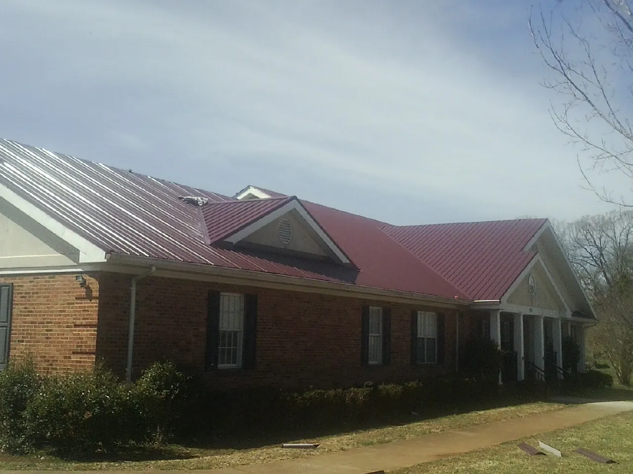 Red metal roof with gabled entries on a long brick building, from a Hail Damage Roof Repair job in Metuchen