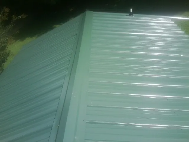 New green metal panels meeting at the ridge of a roof — Flat Roof Repair work by our crew in Metuchen
