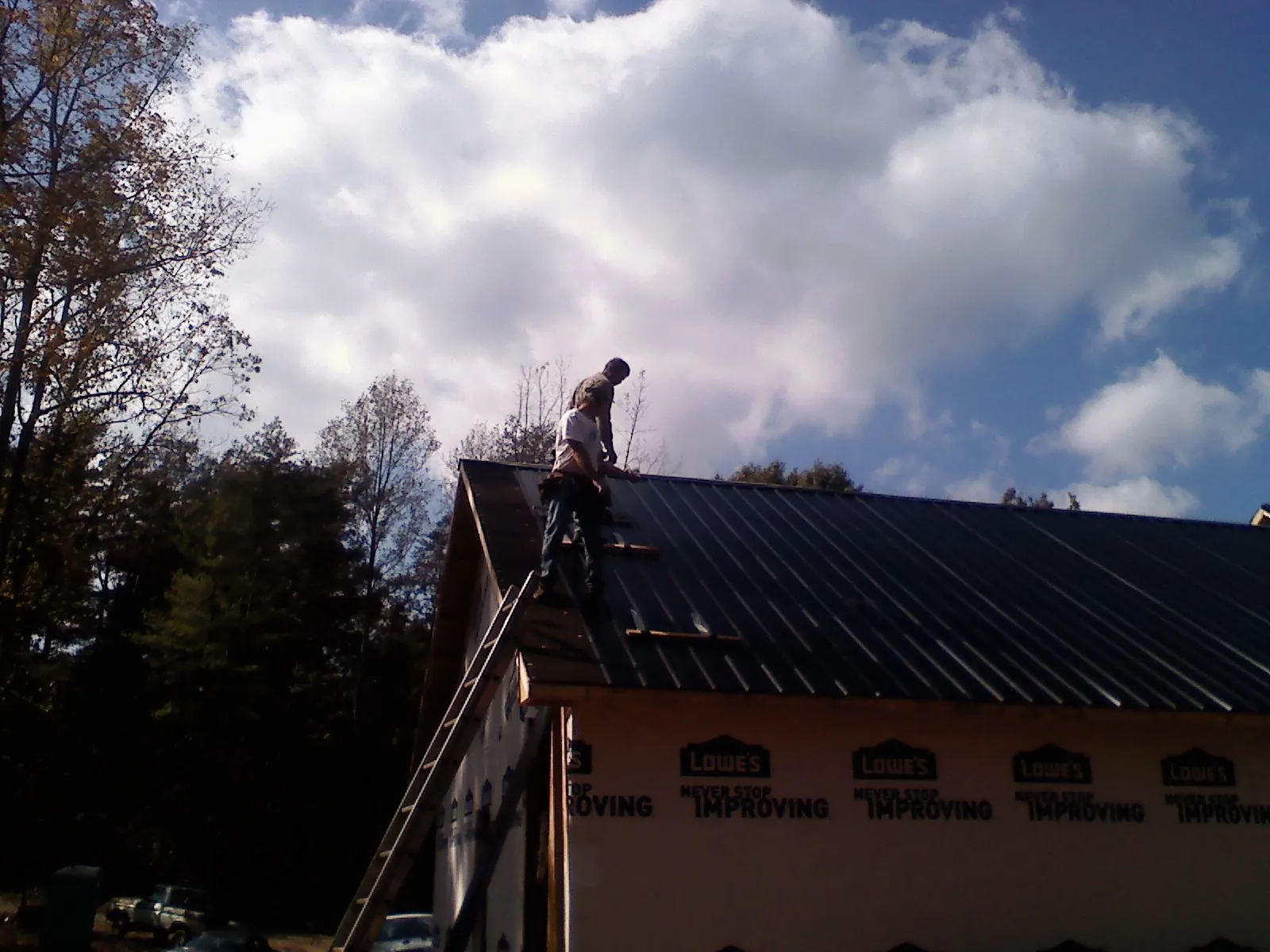 Roofer fastening dark metal panels high against a cloudy sky, from a Roof Inspection job in Metuchen