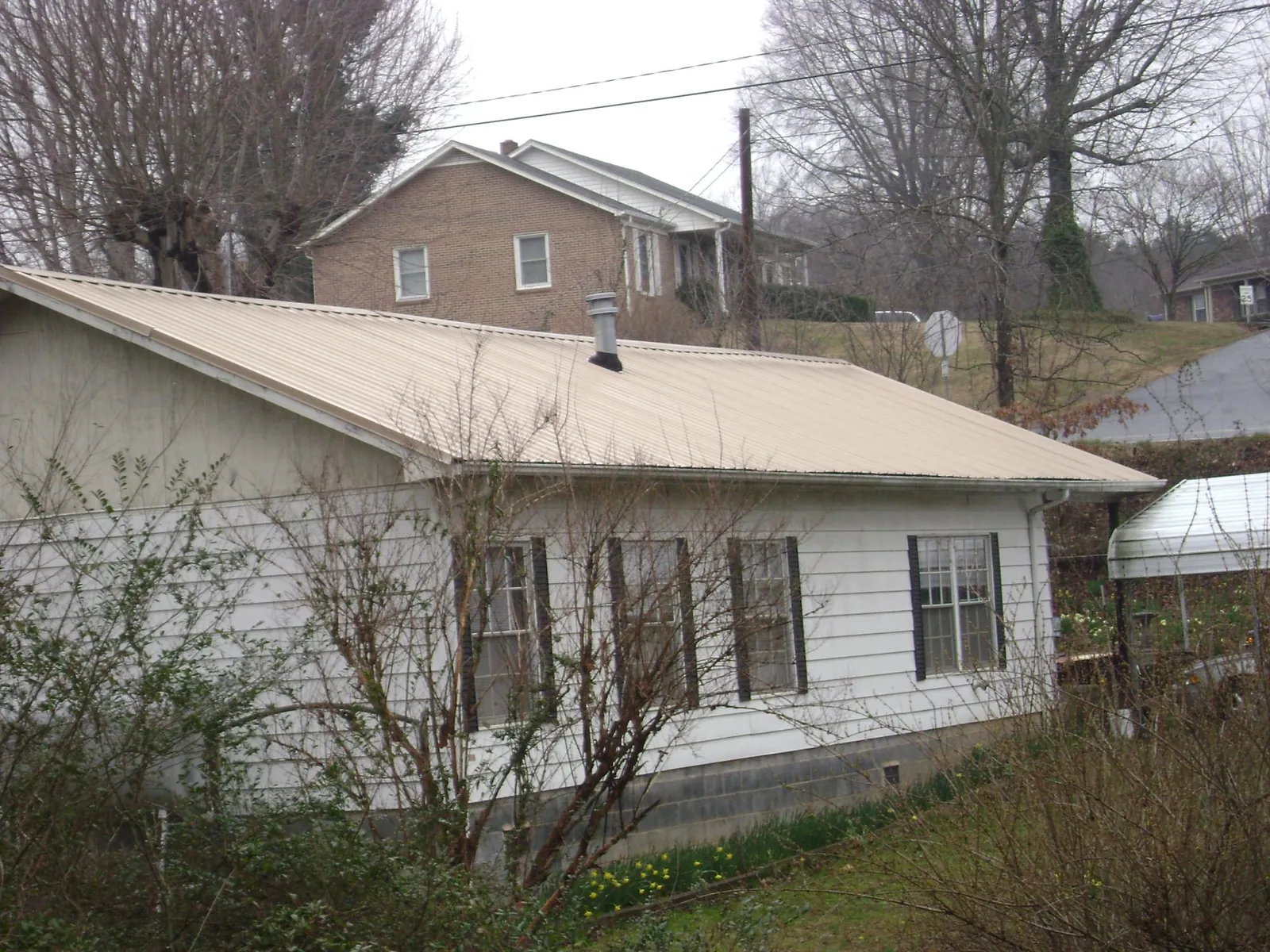 Tan metal roof on a white sided house set into a hillside — Commercial Roofing by Roofing Brothers in Metuchen